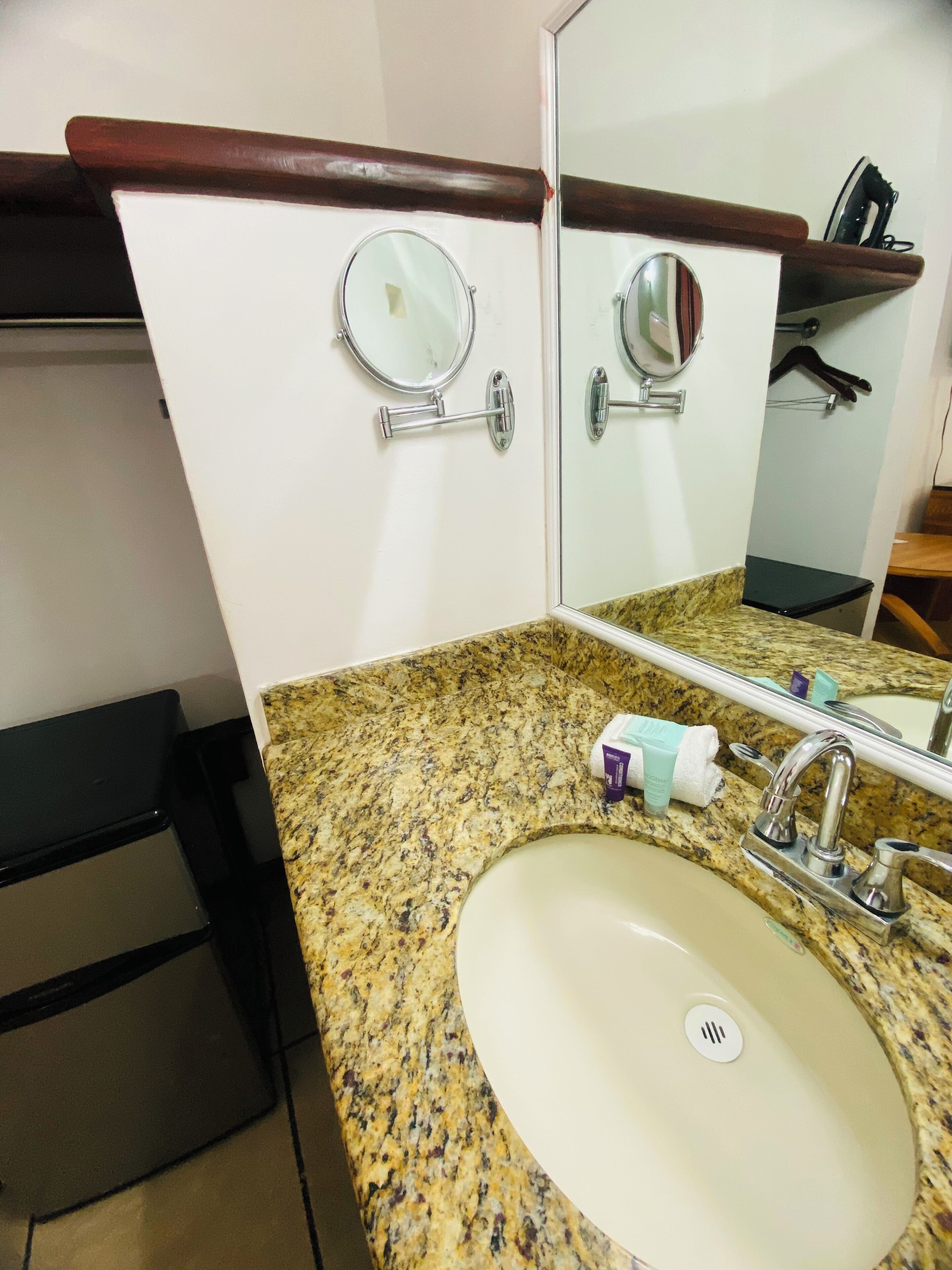 Une salle de bain avec un comptoir en granit, un lavabo blanc, un miroir et une étagère en bois au-dessus du miroir.