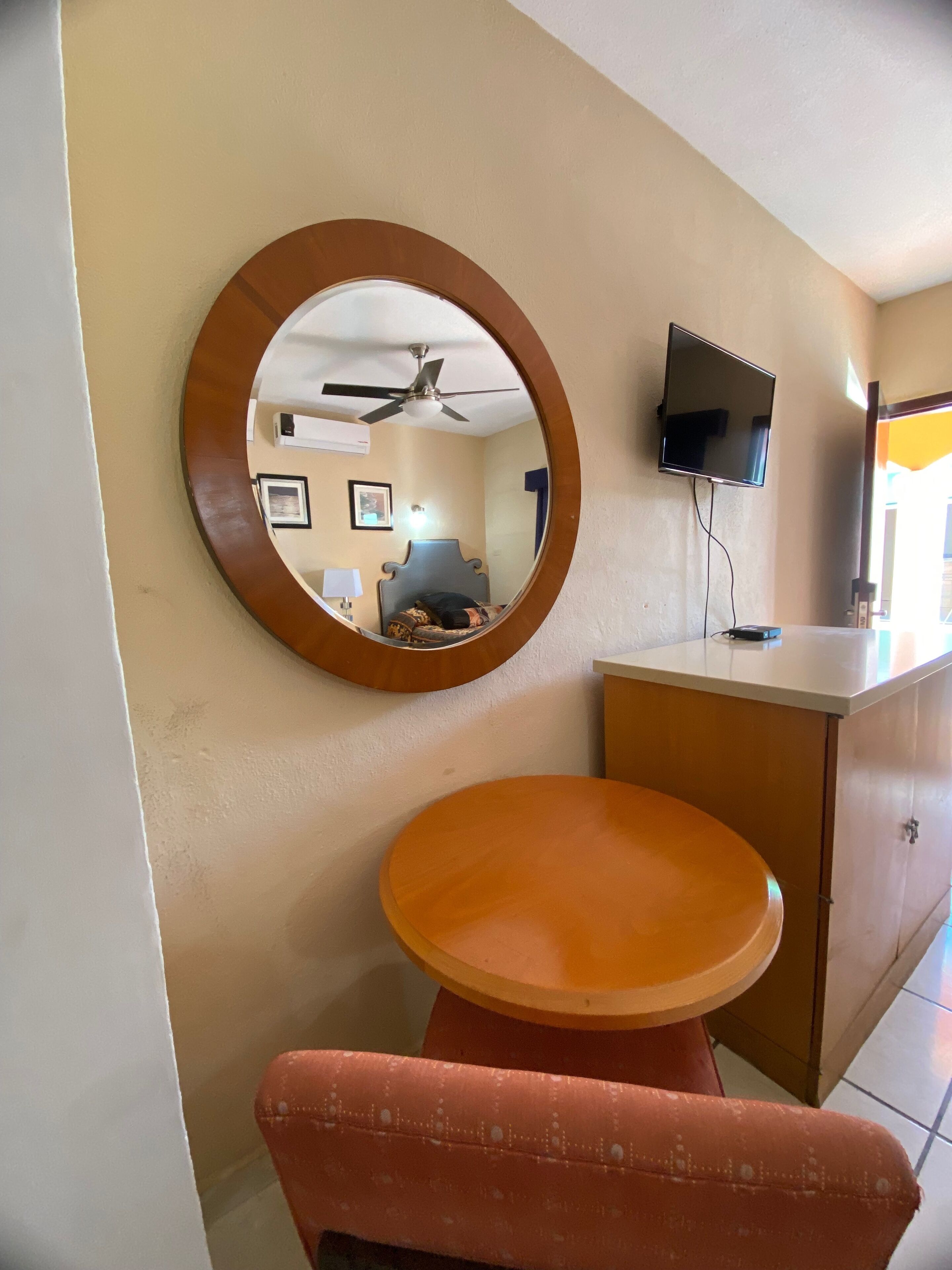 Una habitación con un espejo redondo, un ventilador de techo, una cama, un televisor y una mesita.