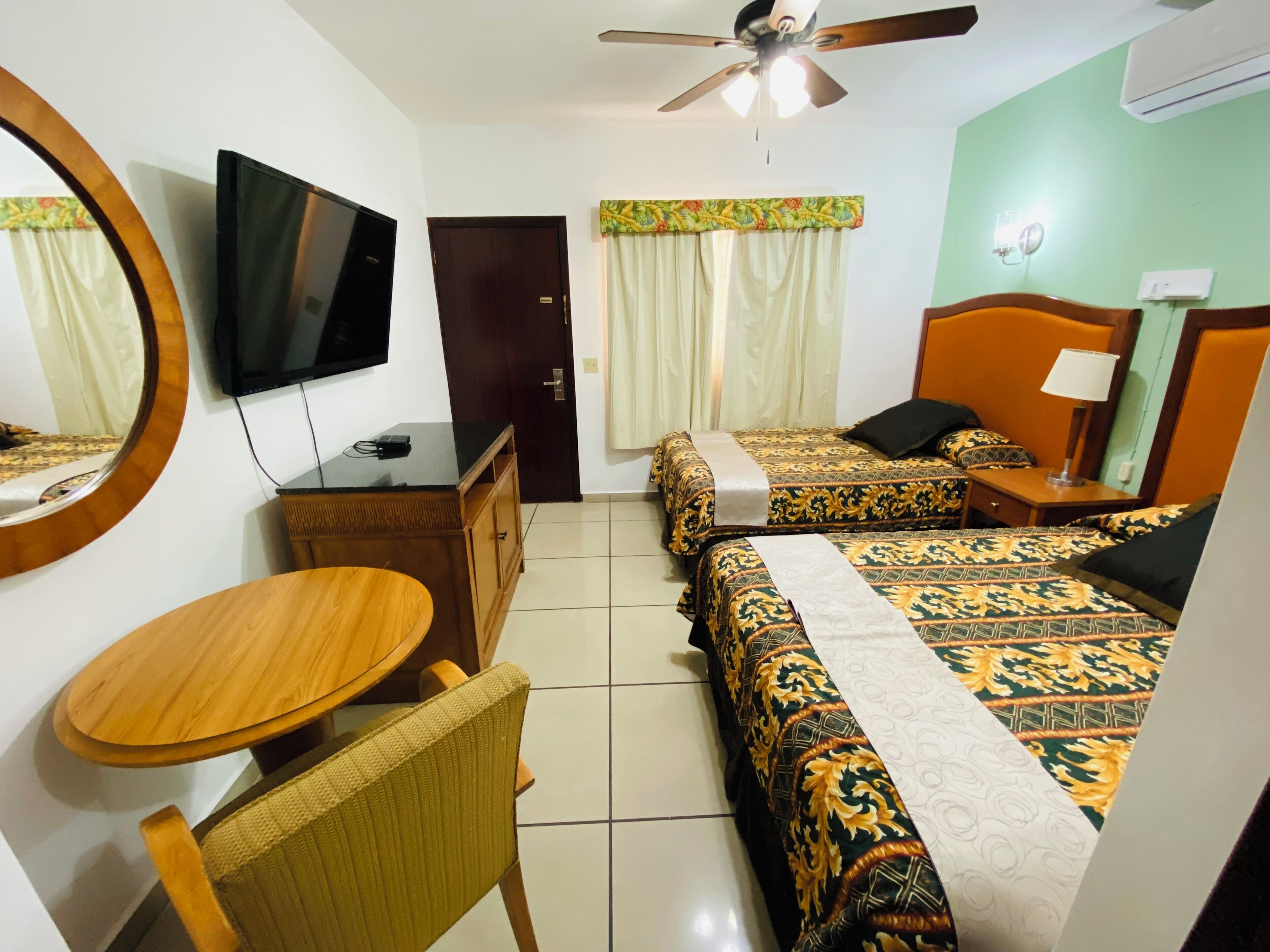 A hotel room with a bed, a desk, a chair, a television, a ceiling fan, and a window with curtains.