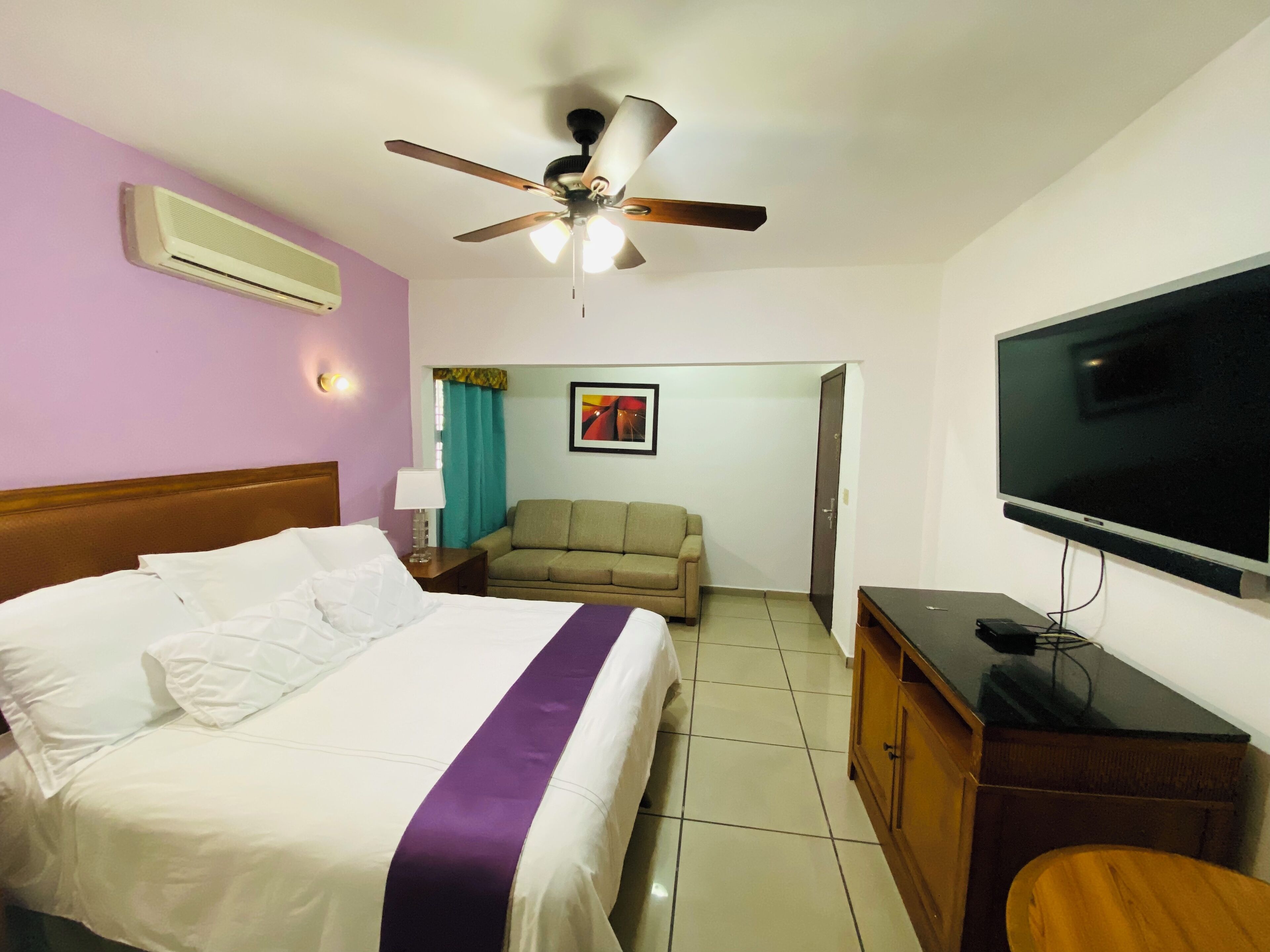A hotel room with a bed, a ceiling fan, a television, and a sofa.