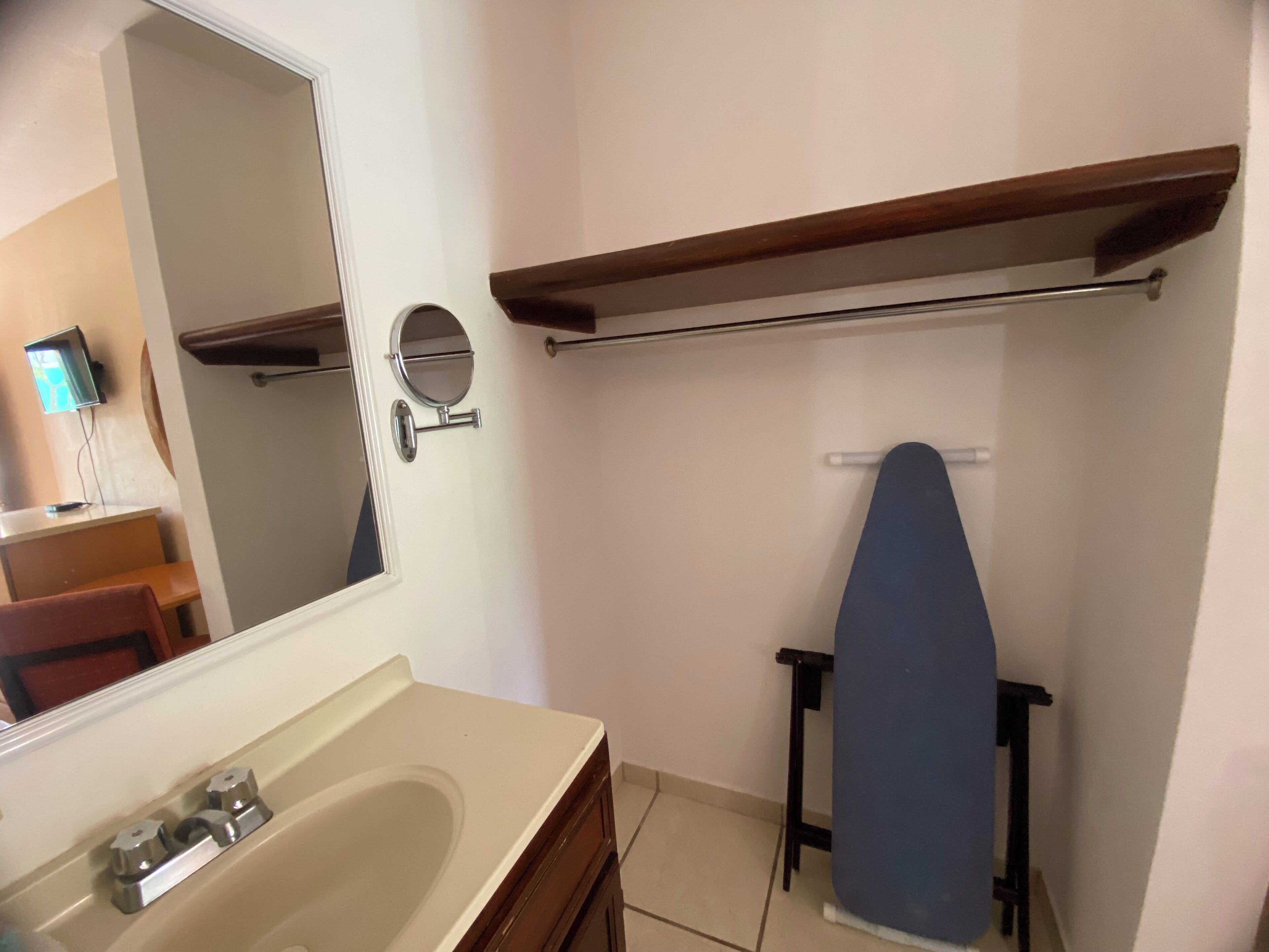 A bathroom with a sink, mirror, and a blue ironing board.