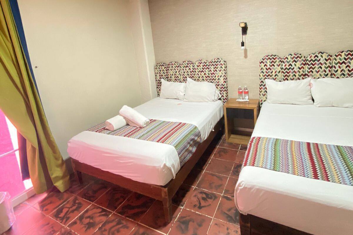 A hotel room with two beds, a nightstand, a lamp, and a window with curtains.
