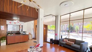 A spacious lobby with a modern chandelier, a reception desk, a sofa, and large windows offering a view of the outdoors. - Hotel Flamingos (Guadalajara)
