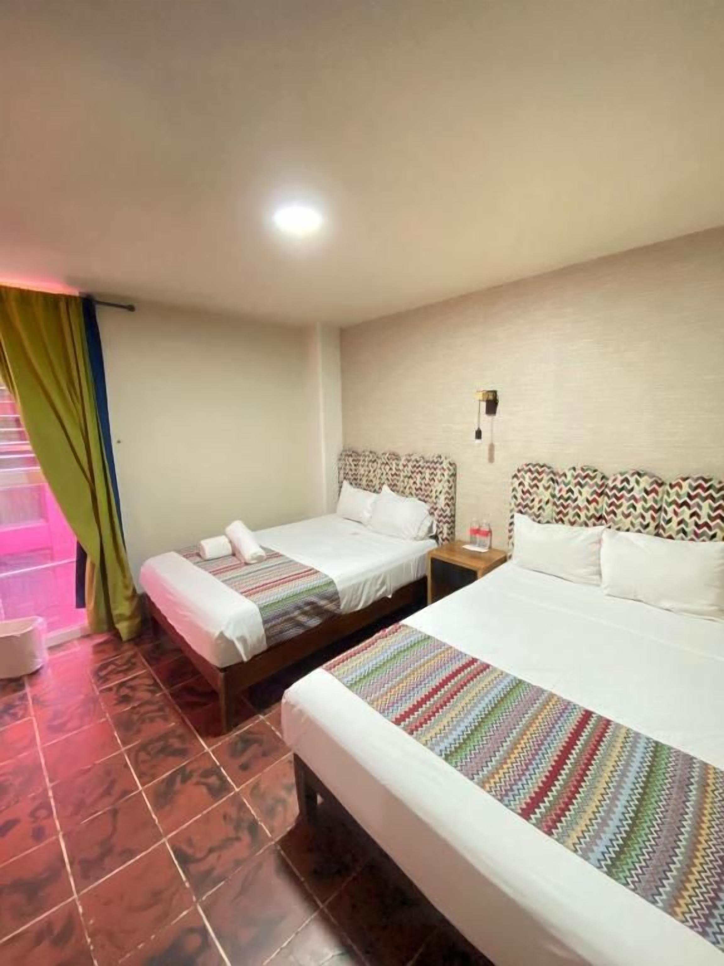 A hotel room with two beds, a nightstand, and a wall-mounted lamp.