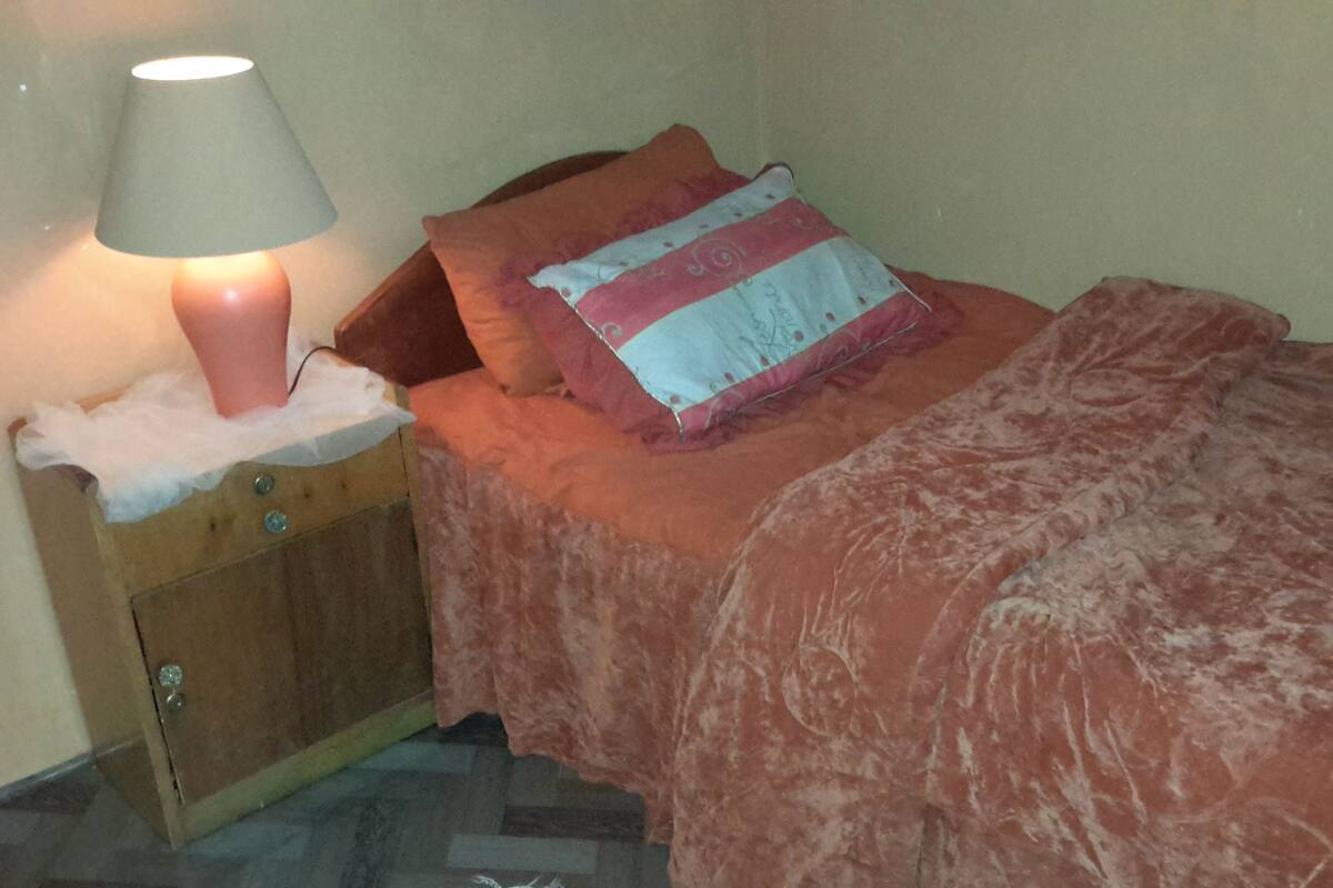 A bedroom with a bed, a nightstand with a lamp, and a wooden cabinet.