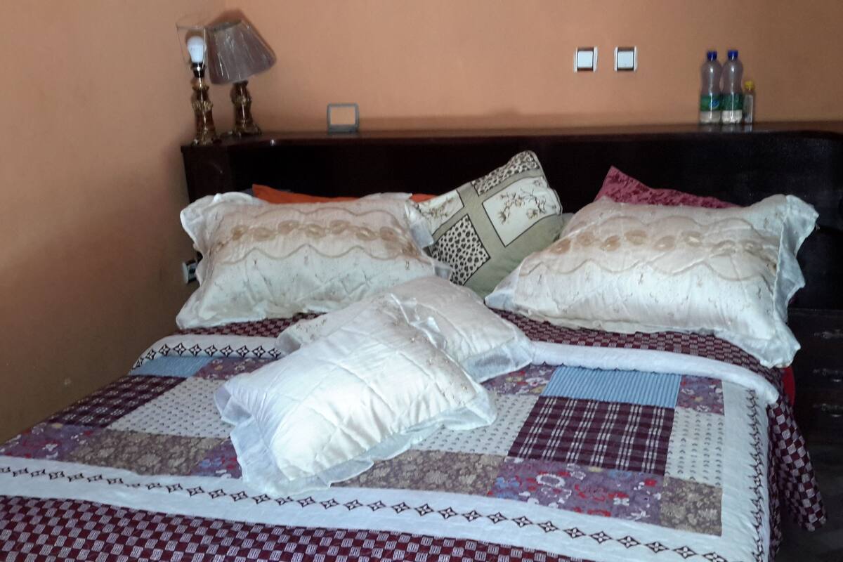 A bed with a quilt, pillows, and a wooden headboard. There are two bottles on the headboard and a lamp on the nightstand.
