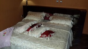 A bed with a white bedspread and red pillows, a wooden headboard, and a wall socket. - Freedom House (Addis Ababa)
