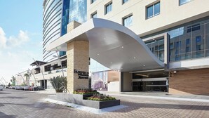 Un hôtel moderne doté d’un auvent incurvé à l’entrée, d’une enseigne bien visible et d’un parking où sont stationnées des voitures.