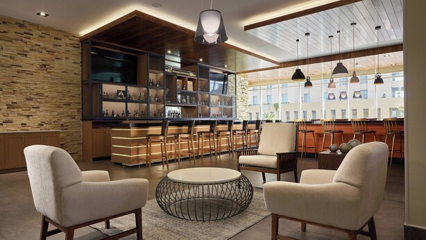 Un espace de détente moderne avec une table basse ronde, deux fauteuils, un bar avec des étagères et une vue sur l’extérieur.