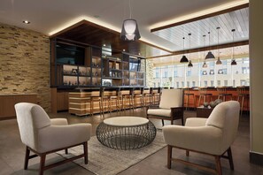 Un espace de détente moderne avec une table basse ronde, deux fauteuils, un bar avec des étagères et une vue sur l’extérieur.