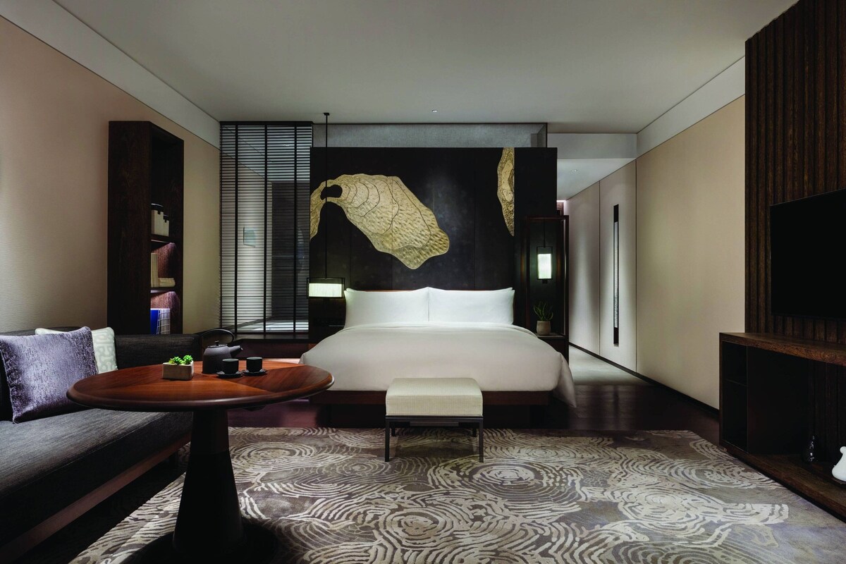 A modern hotel room with a large bed, a sofa, a small table, and a TV.