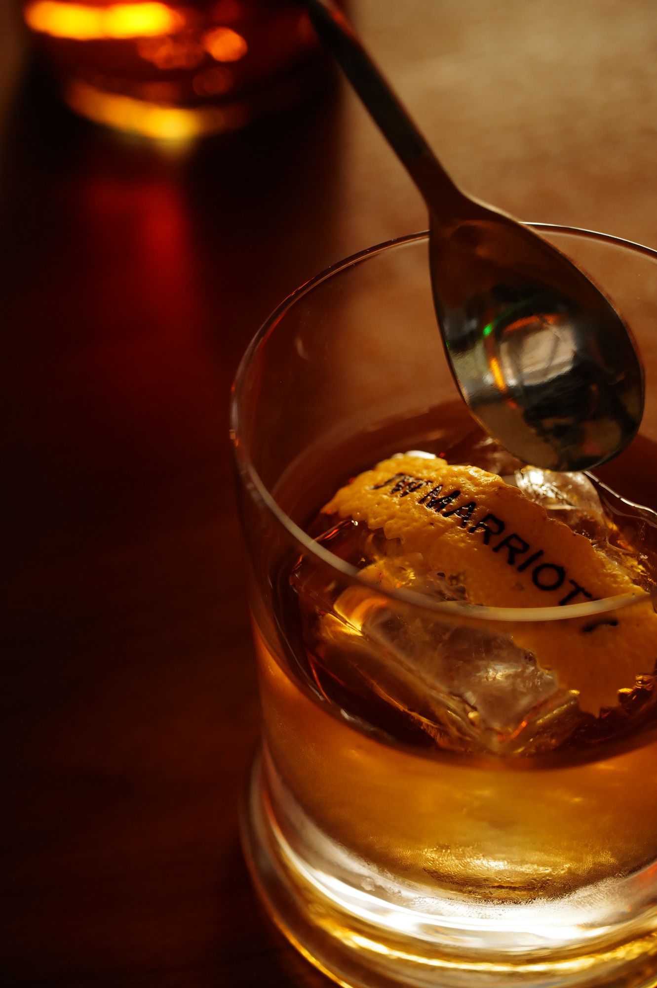 A glass with a golden liquid and ice cubes, with a spoon resting on the rim.