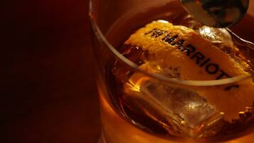 A glass with a golden liquid and ice cubes, with a spoon resting on the rim.