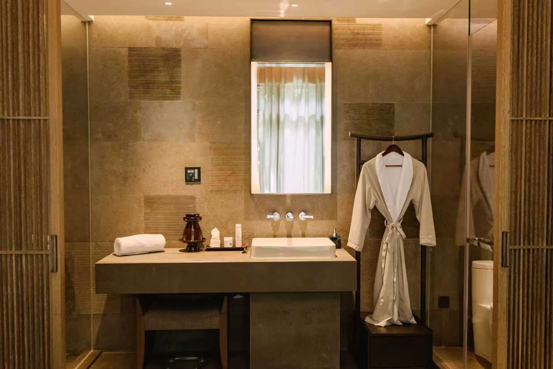 A modern bathroom with a large mirror, a sink, and a robe hanging on a rack.
