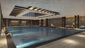 Una piscina interna moderna con soffitto trasparente, aree relax e una parete in pietra.