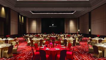 Sala de conferências do JW Marriott com mesas redondas, carpete vermelho e um fundo escuro com o logotipo do hotel.
