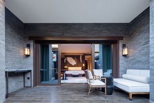 A modern hotel room with a large bed, a seating area with a sofa and chairs, and a fireplace.