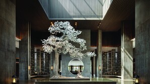 Una hall moderna con una grande scultura arborea, uno specchio circolare e un design minimalista.