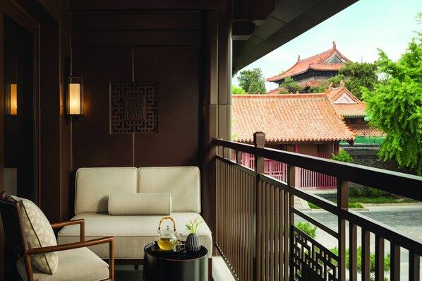 Relax on the balcony with a traditional Asian-style sofa and enjoy the serene views of lush greenery and a nearby building with a tiled roof.