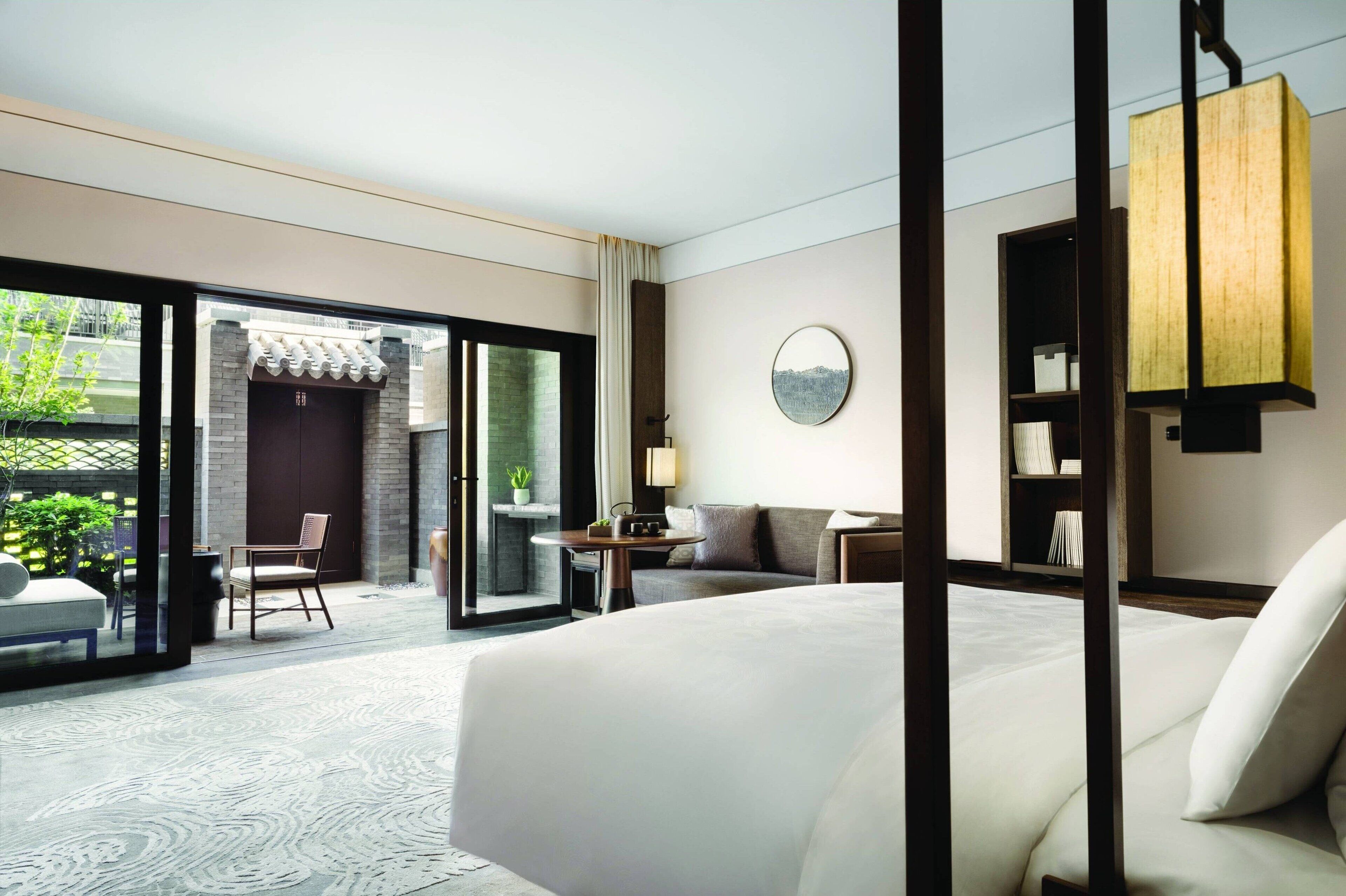 Una habitación de hotel moderna con una cama grande, una mesita pequeña, una silla y vistas al exterior.