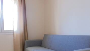 Una habitación con un sofá gris, una ventana con cortinas y un equipo de aire acondicionado en la pared.