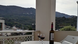 Un balcó amb una taula, dues cadires de plàstic blanc, una ampolla de vi i dues copes de vi.