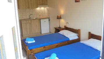 A room with two wooden beds, a small kitchenette, and a single lamp.