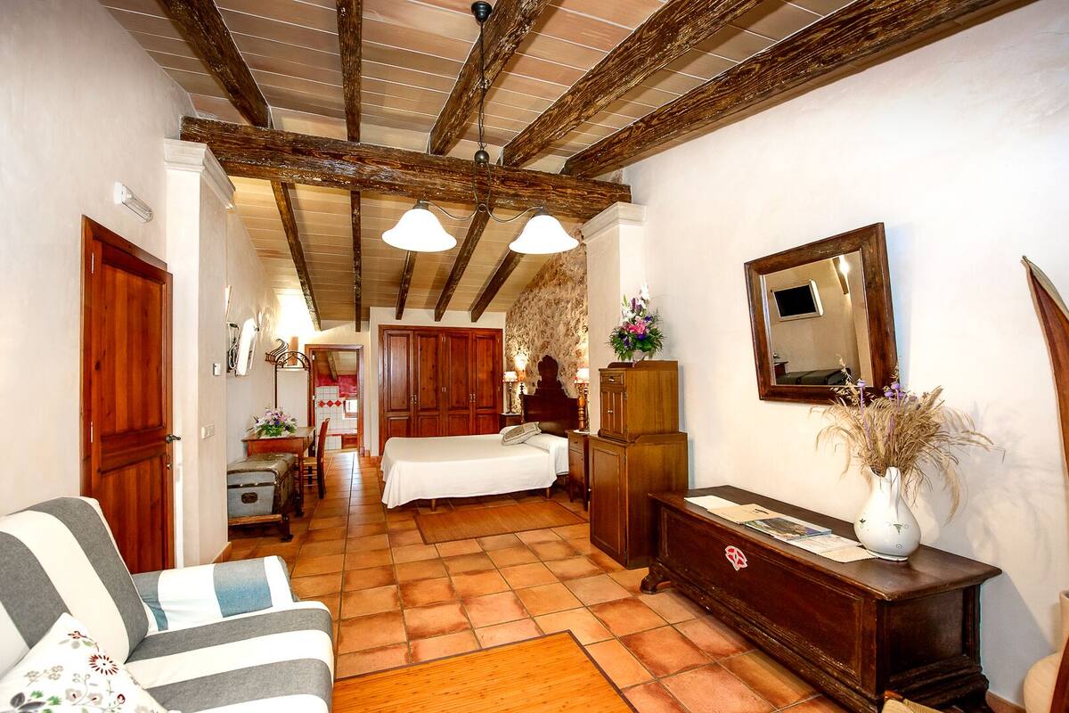 A cozy room with a bed, wooden furniture, a tiled floor, and a wooden ceiling.