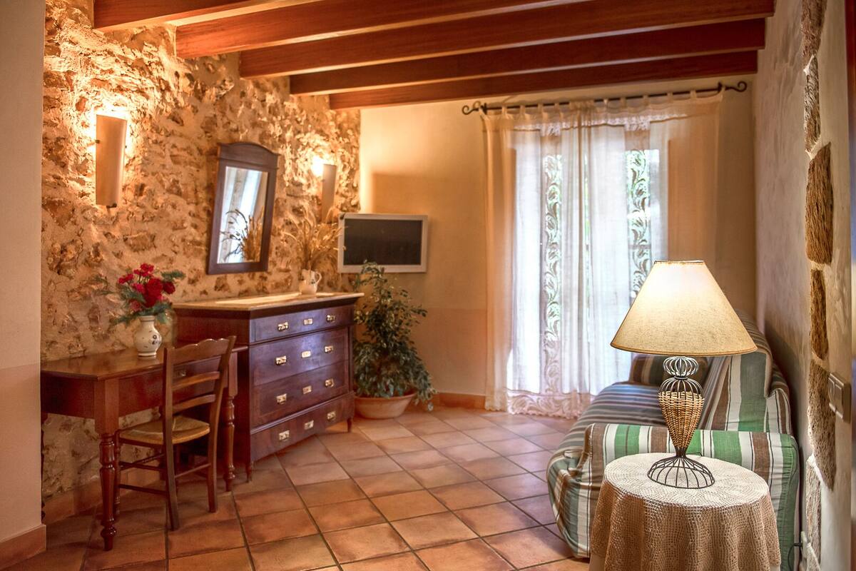 A cozy room with a stone wall, wooden furniture, a television, and a window with curtains.