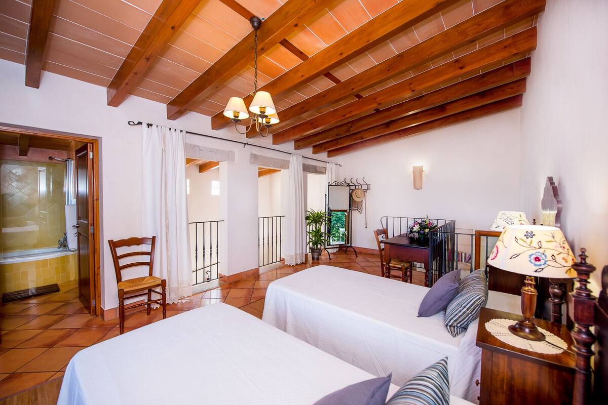 A room with two beds, a dining table, a lamp, and a view of a balcony.
