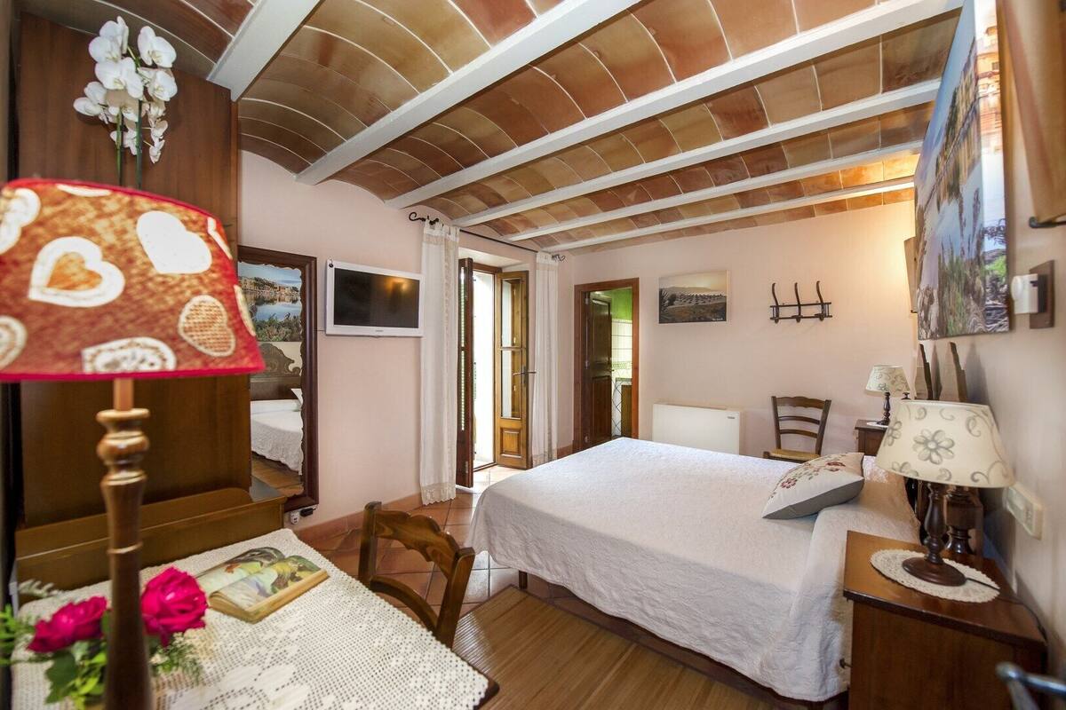 A bedroom with a bed, a desk, a chair, a lamp, and a TV.
