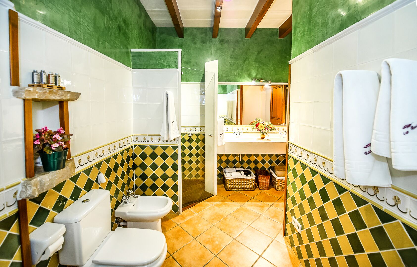 Ein Badezimmer mit Toilette, Waschbecken und Duschbereich, mit grün-gelben gemusterten Fliesen.