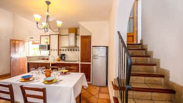 Un coin repas avec une table dressée pour quatre personnes, une cuisine équipée d’un réfrigérateur et un escalier.