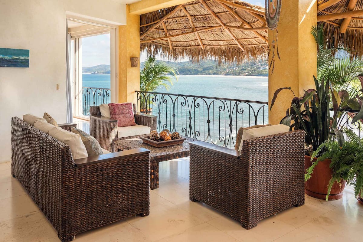 A cozy lounge area with wicker furniture, a thatched roof, and a view of the sea.