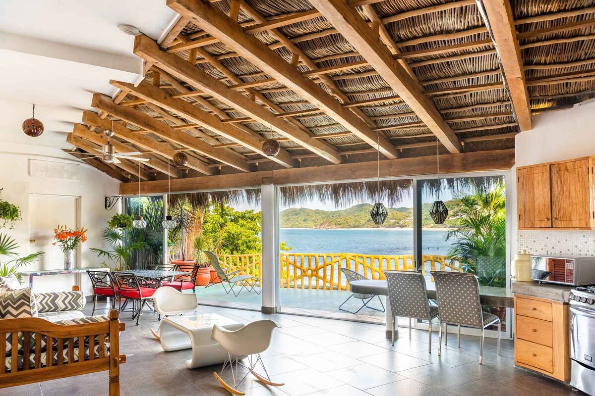 A spacious living area with a view of the sea, wooden ceiling beams, and modern furniture.