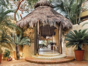 A thatched-roof structure with a circular staircase leading to a covered area, surrounded by palm trees and potted plants. - Villa Amor (Sayulita)
