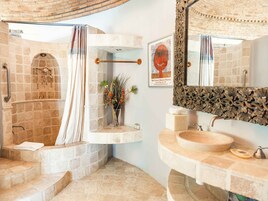Un baño con ducha de piedra, lavabo de madera y espejo con marco decorado.