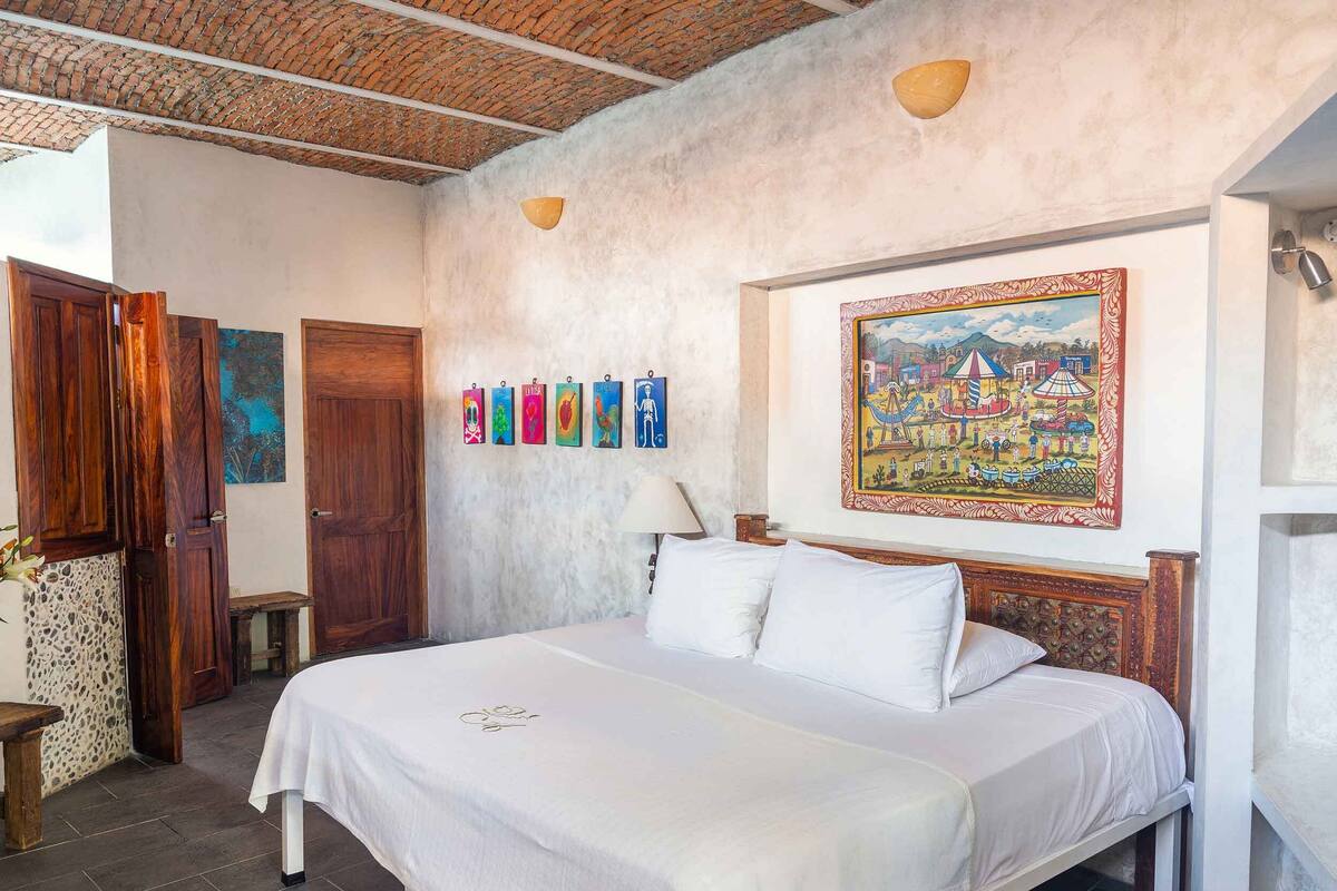 A bedroom with a bed, a wall with a framed painting, and a door.