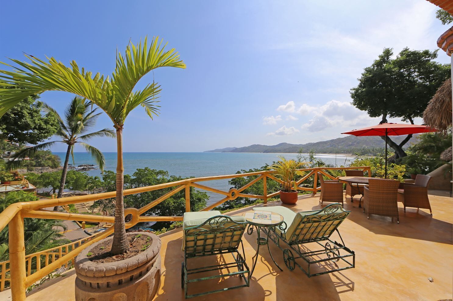 Una terraza con mesas al aire libre, una palmera y vista al mar.