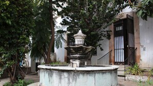 A fountain in a courtyard surrounded by trees and a building with barred windows.