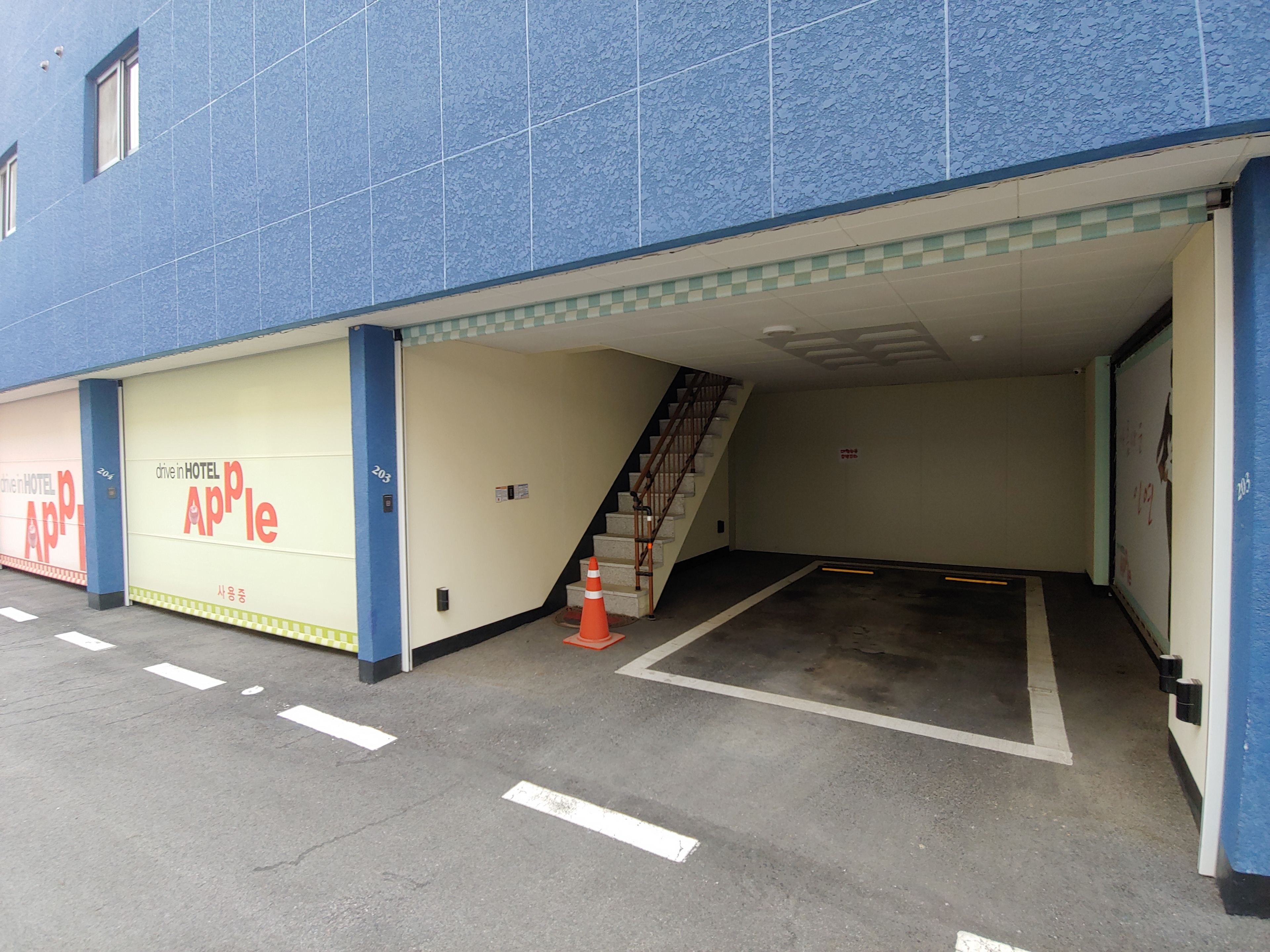 Un estacionamiento de hotel con fachada azul y acceso vehicular.