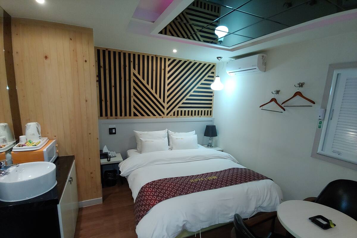 A hotel room with a bed, bedside table, lamp, and a small round table with a chair.