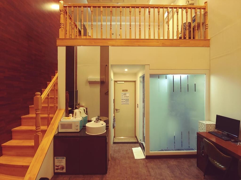 A hotel room with a wooden staircase, a kitchenette, a shower area, and a desk with a computer.