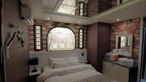 A hotel room with a bed, a nightstand, a desk with a microwave, a sink, and a large mirror. There are two windows with decorative frames and a skylight above the bed. - Apple Drive-in Motel (Yeoju)