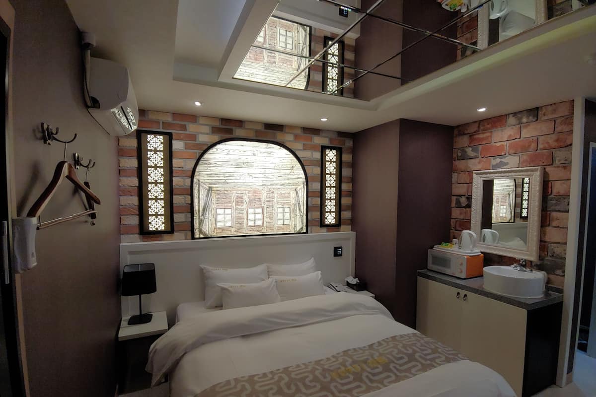 A bedroom with a bed, a nightstand, a dresser, a mirror, and a window with a view of a building.