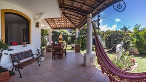 Eine überdachte Terrasse mit Tisch, Stühlen, einer Hängematte und einer Statue.