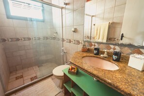 Un baño con ducha envuelta en vidrio, inodoro, lavamanos con encimera de granito y espejo sobre el lavamanos.