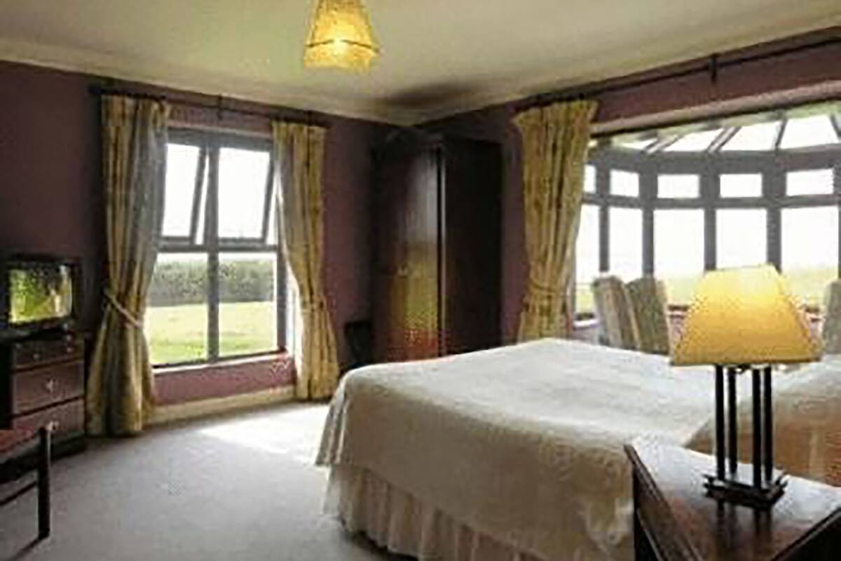 Een slaapkamer met een groot bed, een bureau met een lamp, een televisie en een raam met gordijnen.