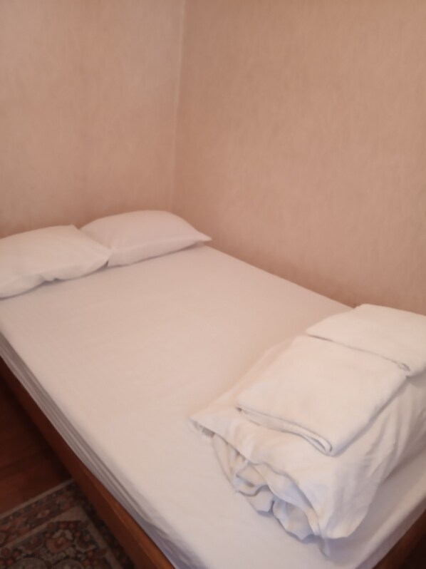 Una cama individual con ropa de cama y almohadas blancas, un cabecero de madera y un tapete estampado en el suelo.