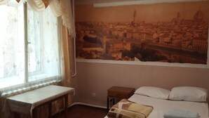 A bedroom with a bed, a nightstand, a desk, and a window with curtains. - Kok-Tobe Almaty Hotel (Almaty)